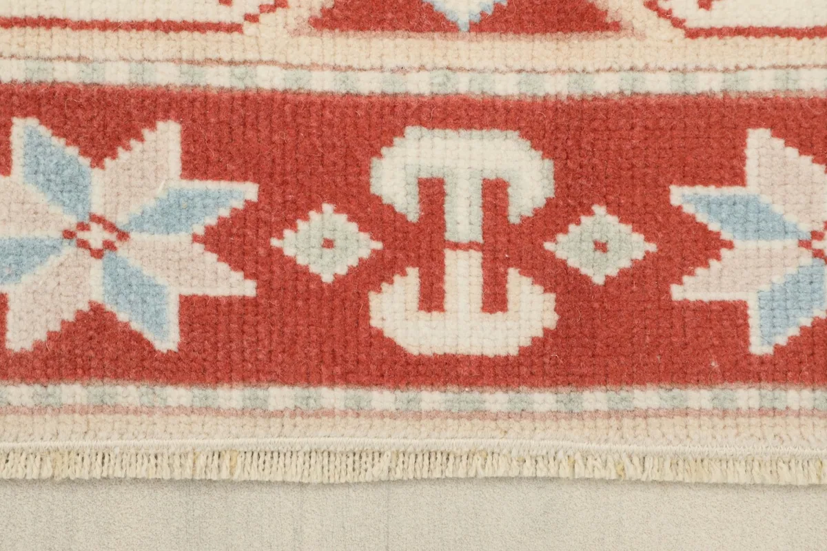 Close-up of the rug's red border with blue and ivory star and geometric elements