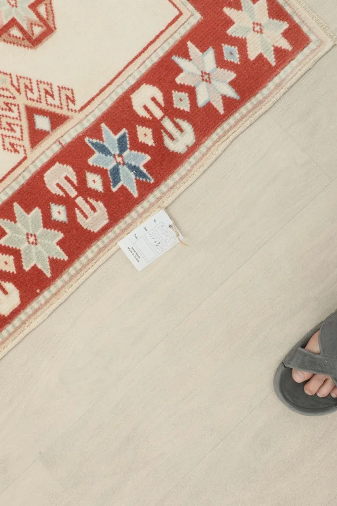 Top-down view of the rug's end with a tag, next to a person's foot in a sandal