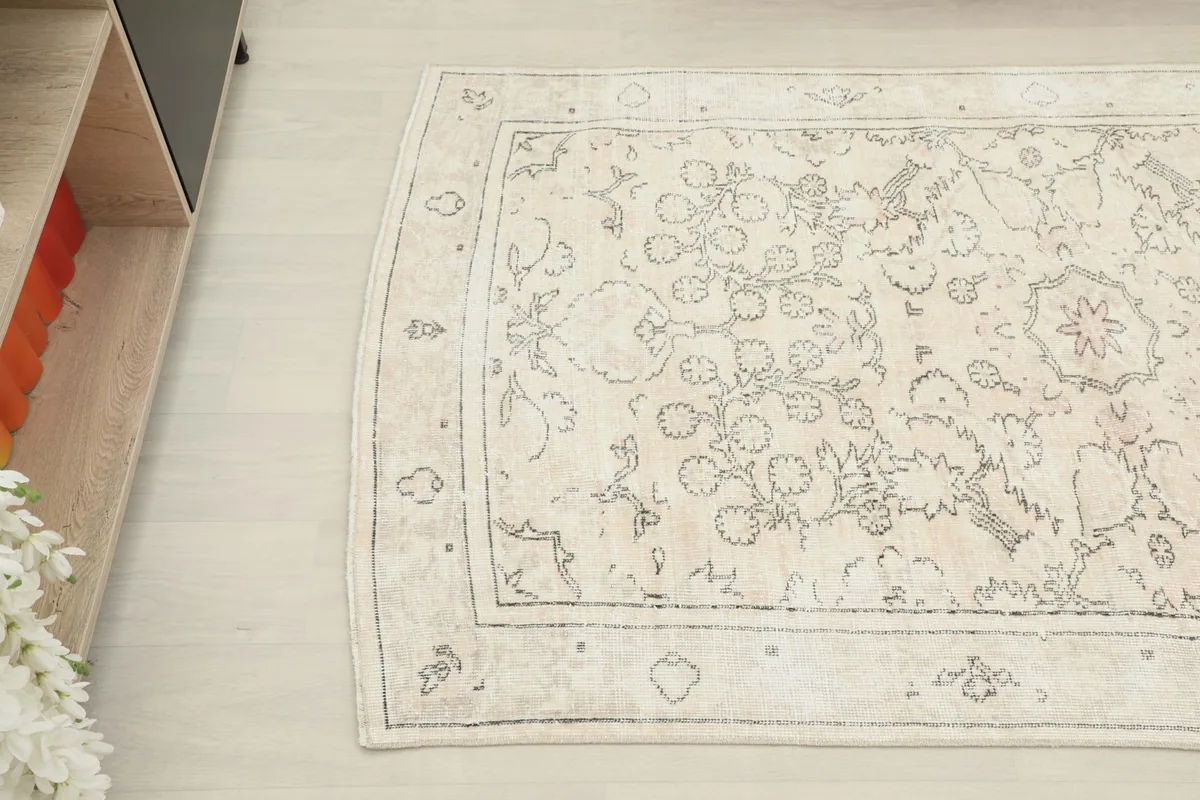 Overhead view focusing on the upper left half of the beige rug, showing detail near furniture
