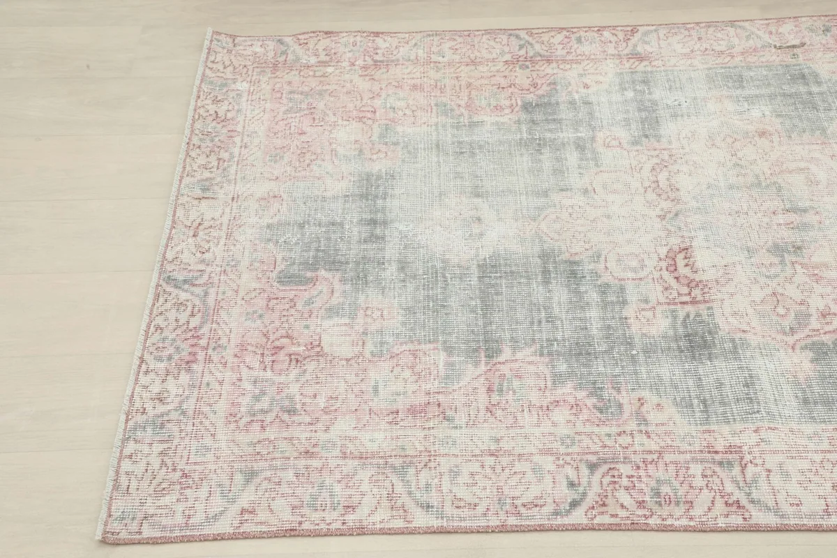 Angled close-up of the vintage rug's corner, detailing the distressed rose and gray patterns