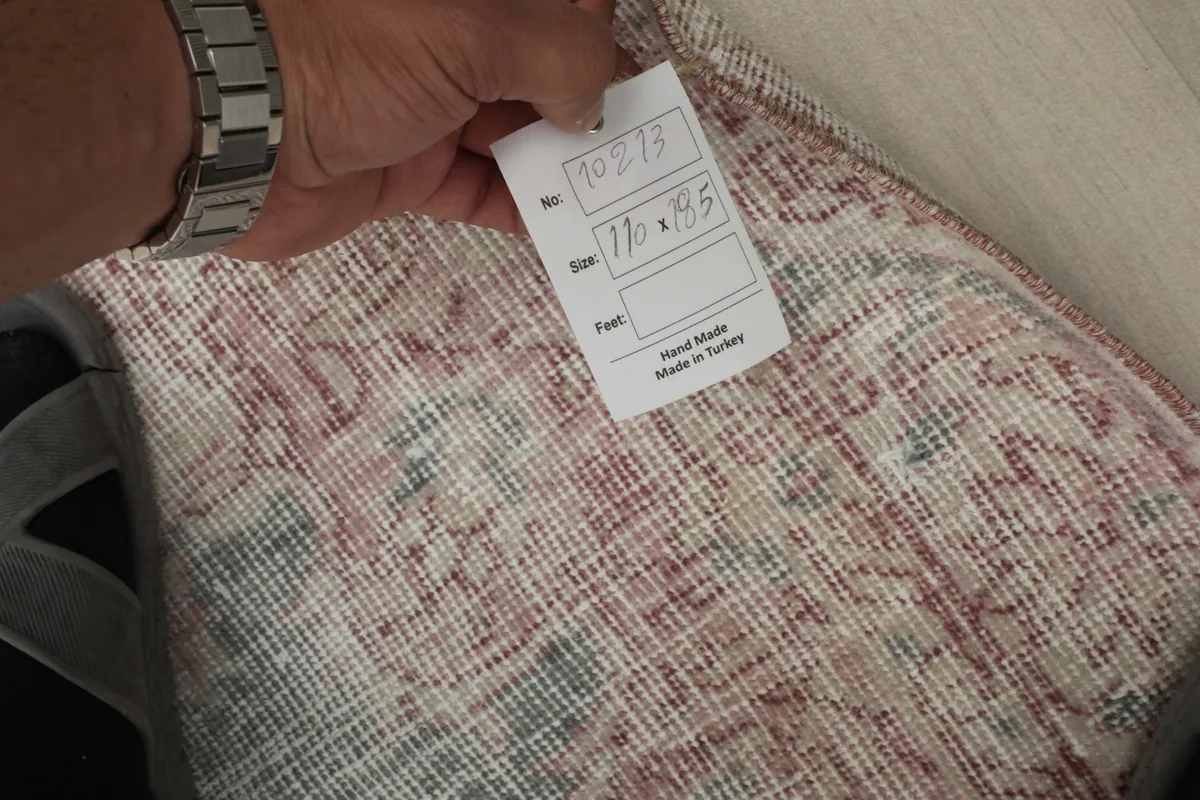 Hand holding a tag with the rug's dimensions and 'Hand Made in Turkey' on the reverse side