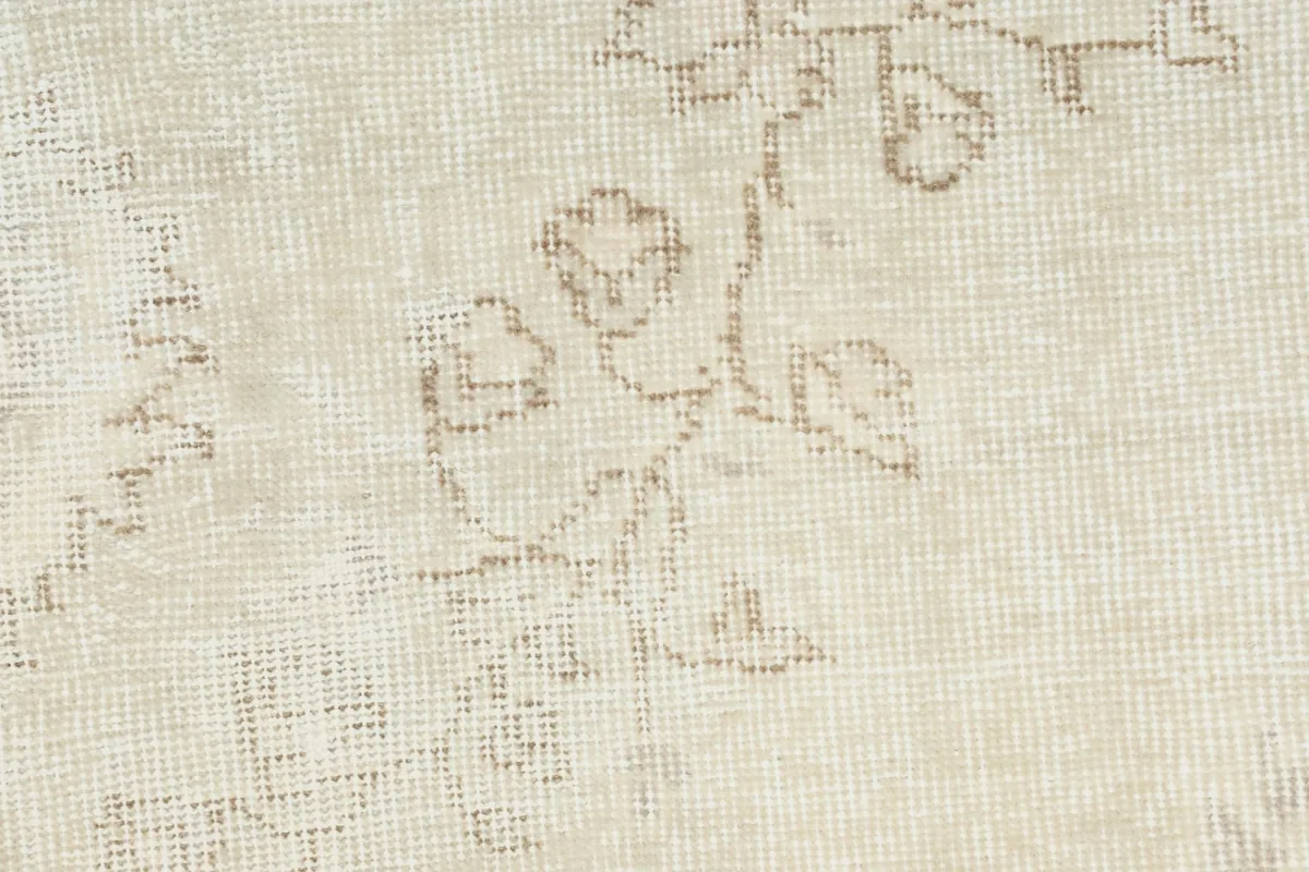 Detailed close-up of the hand-knotted wool pile and faded floral pattern in beige