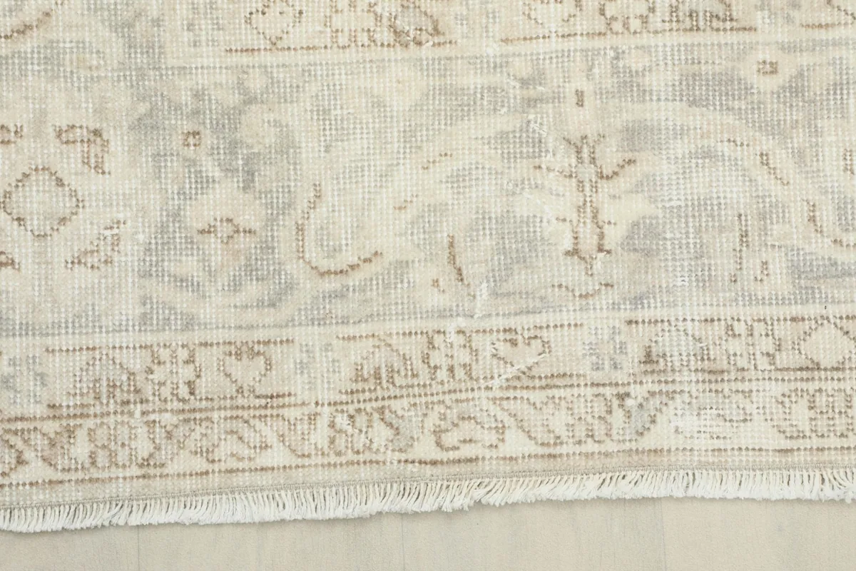 Close-up of the rug's border, showing the intricate, faded design and fringe