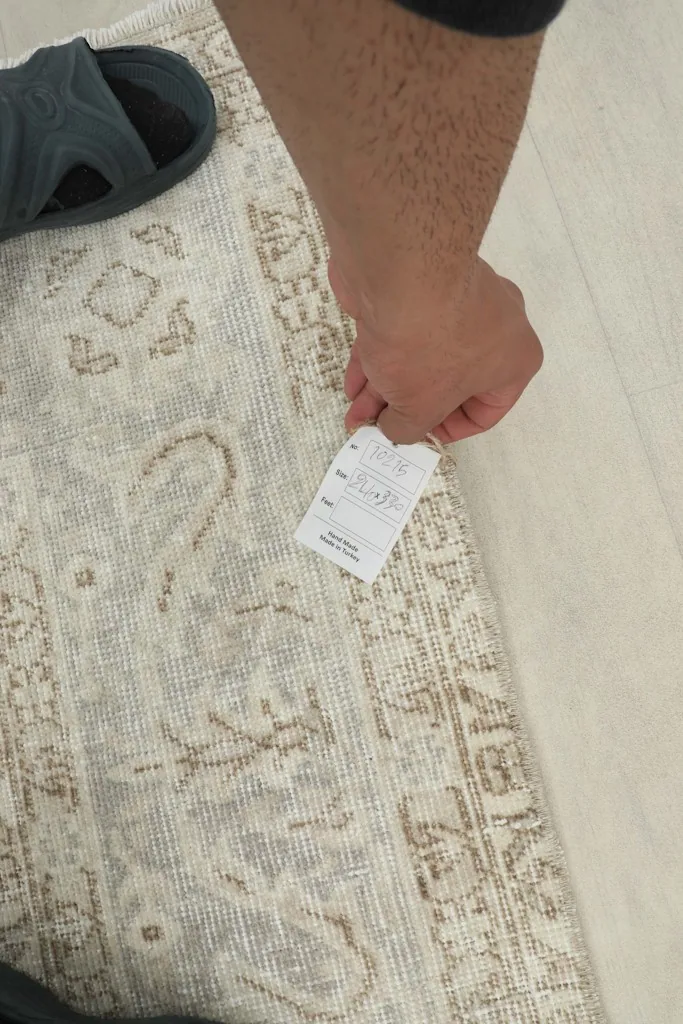 A hand holding a small tag near the rug's border, showing the texture and low pile