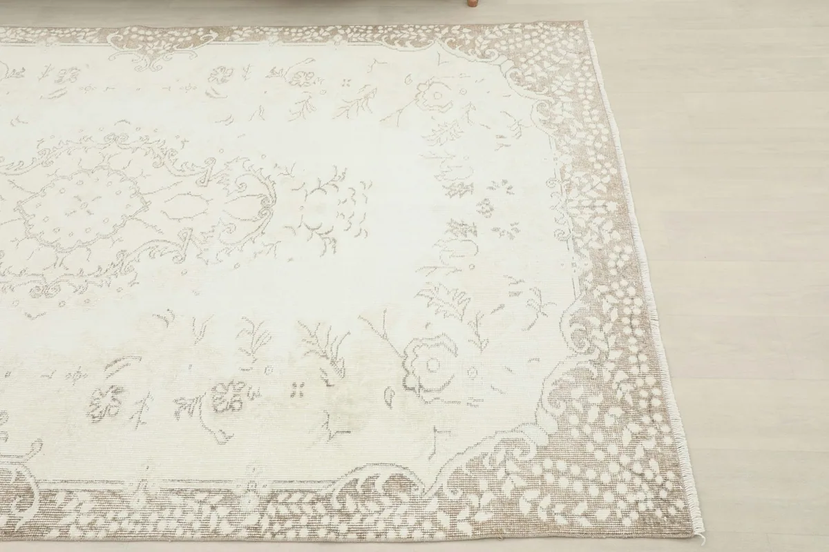 Close-up detail of the corner of the rug, showing the faded beige floral border against the ivory field.