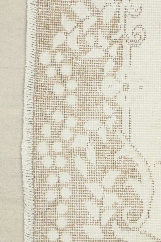 Detailed view of the rug's edge, showcasing the patterned beige border and the hand-finished fringe.