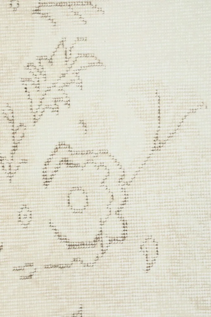 Extreme close-up of the rug's low wool pile, revealing the hand-knotted texture and faint floral motifs.