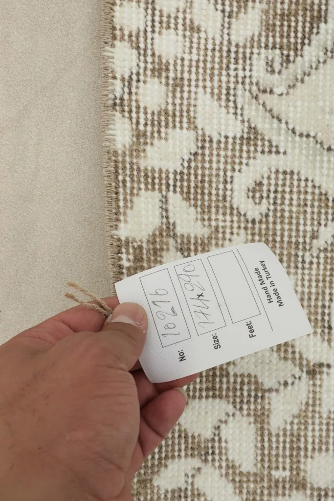 Hand holding a tag against the back of the rug, showing the details of its hand-knotted construction.
