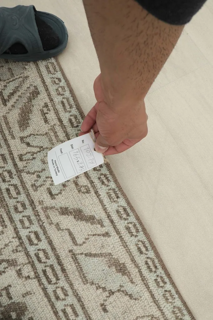 Hand holding a label near the rug border, showing the fine details of the pattern
