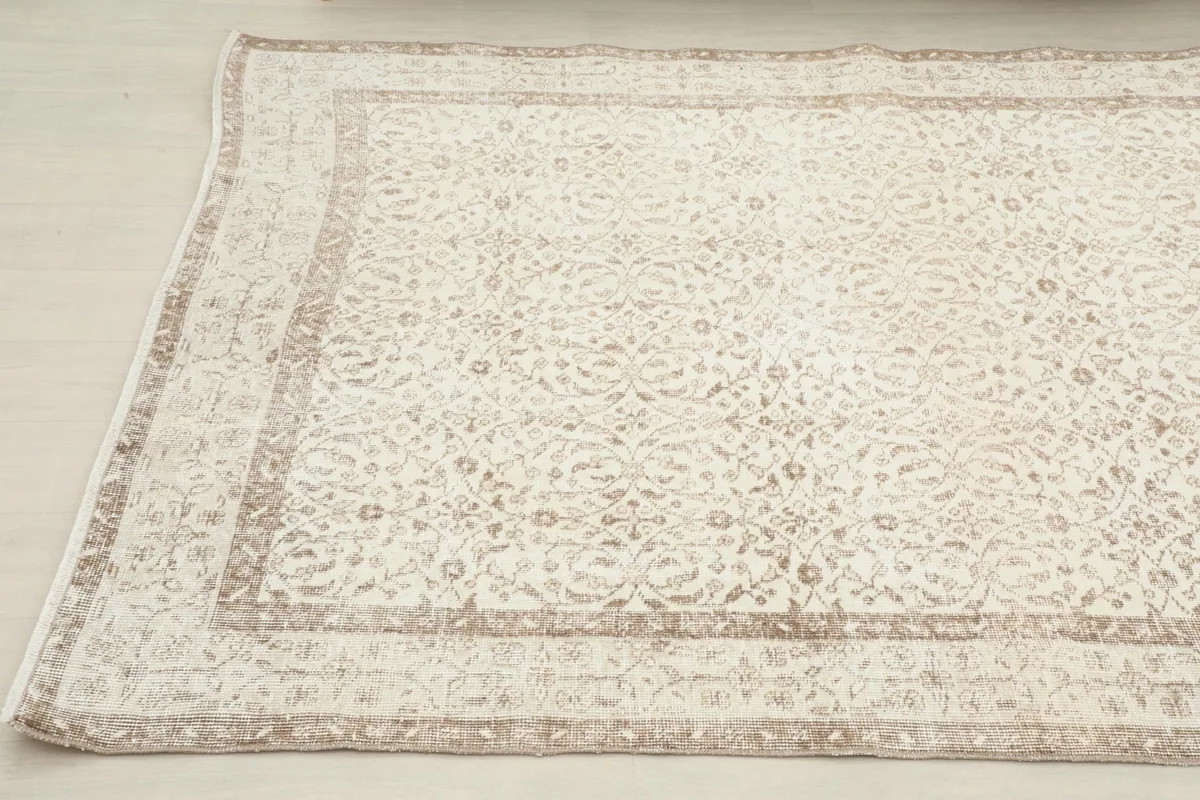 Close-up angled view of the ivory and beige vintage rug, highlighting its full design