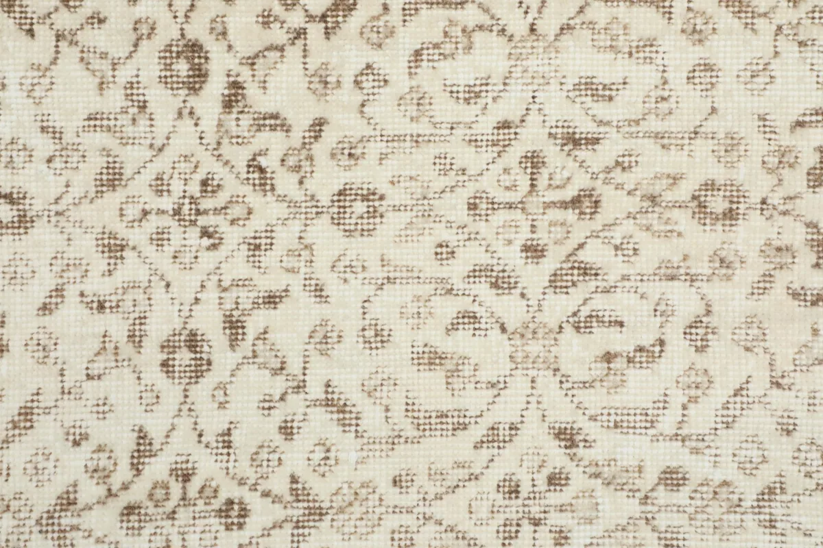 Tight close-up of the hand-knotted wool pile, showing the beige floral patterns on an ivory ground