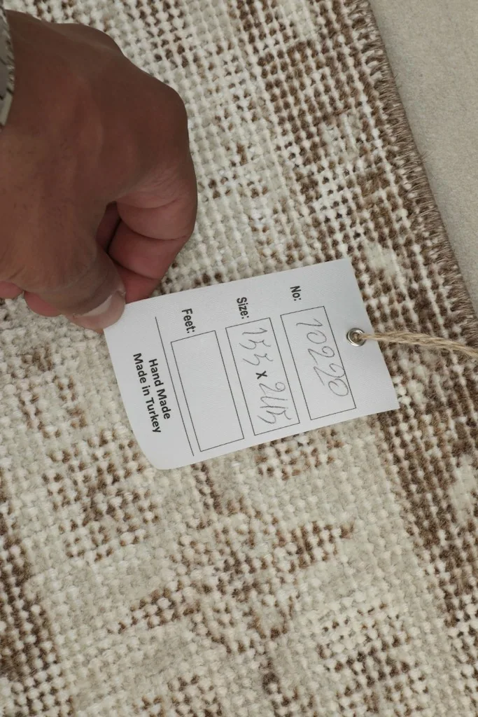 Hand holding a tag showing the rug's dimensions and origin, confirming it is hand made in Turkey