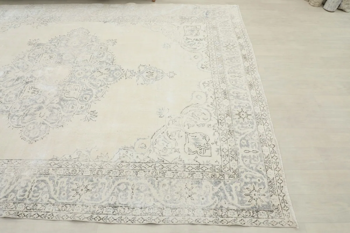 Close-up angled view showing the corner of the ivory rug with its faded charcoal geometric border design.