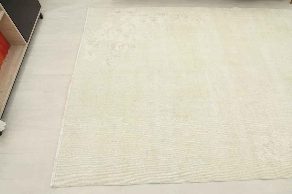 Angled view of the rug's edge next to furniture, highlighting its cream color