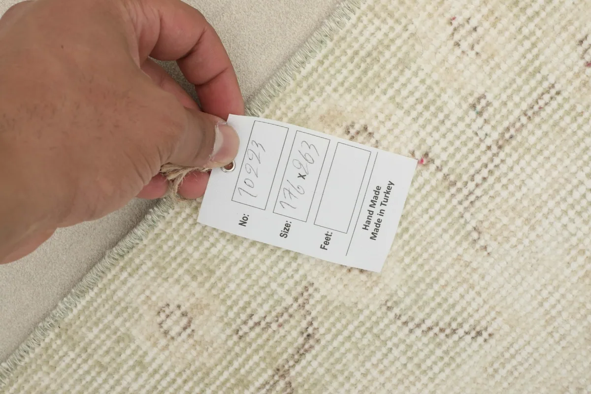 Hand holding a product tag with size and origin information on the rug's back