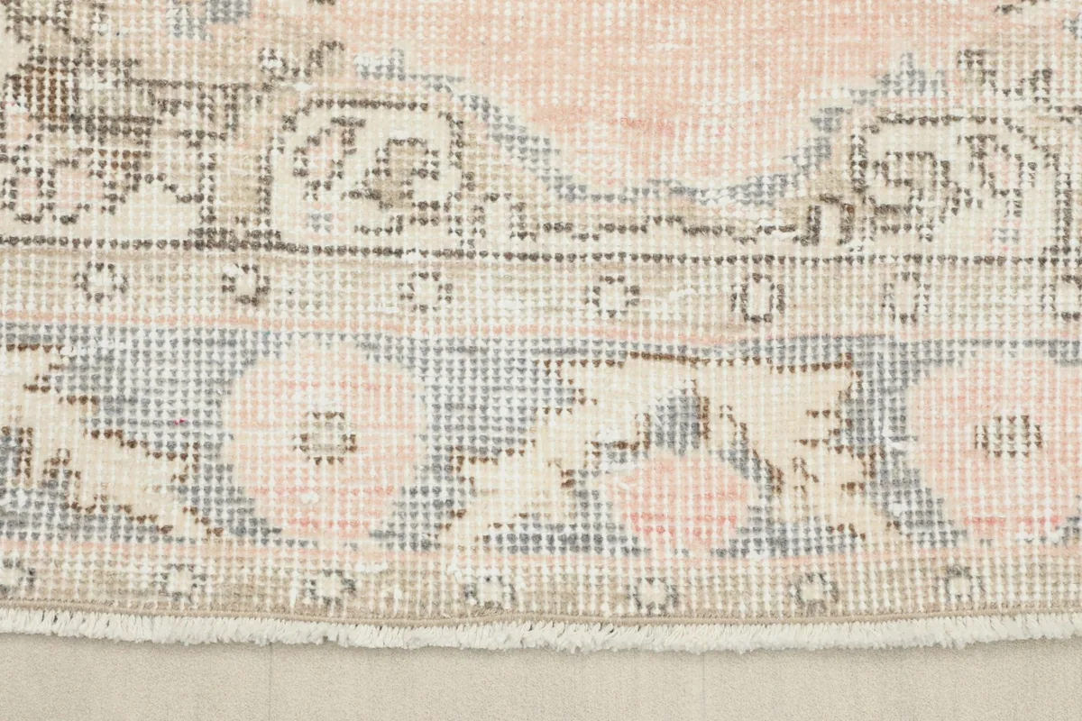 Close-up of the rug's border, showcasing the floral motifs in rose and gray, and the fringe.