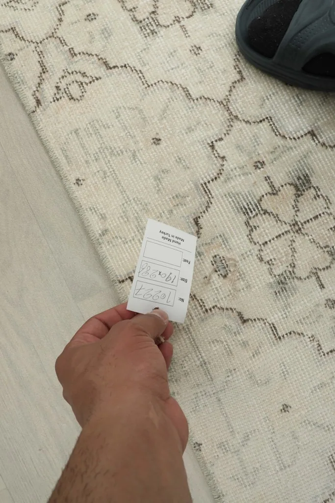 Hand holding a tag on the rug's surface, showing scale and texture