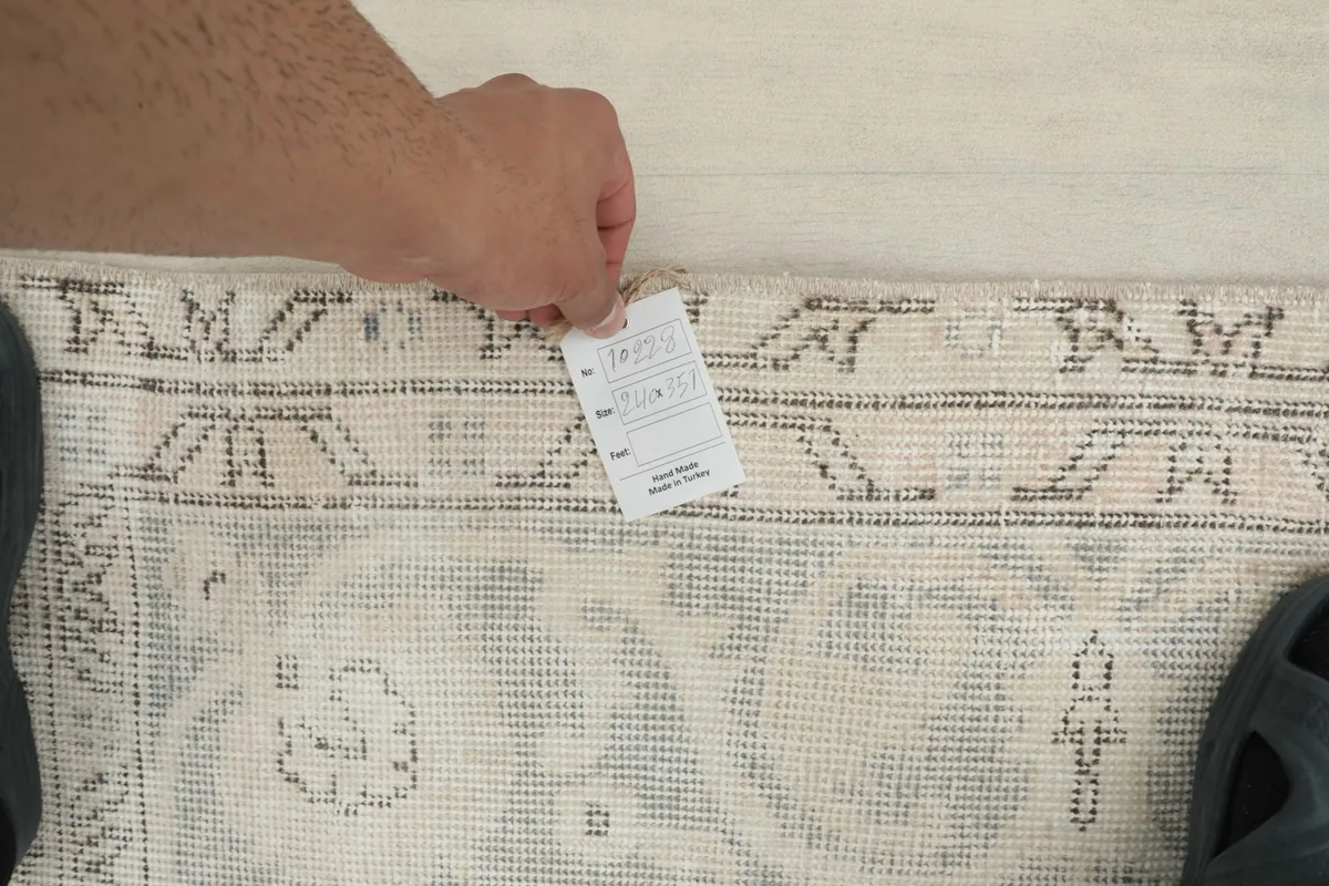 Person's hand holding a tag near the rug's edge, showing the texture and tag details