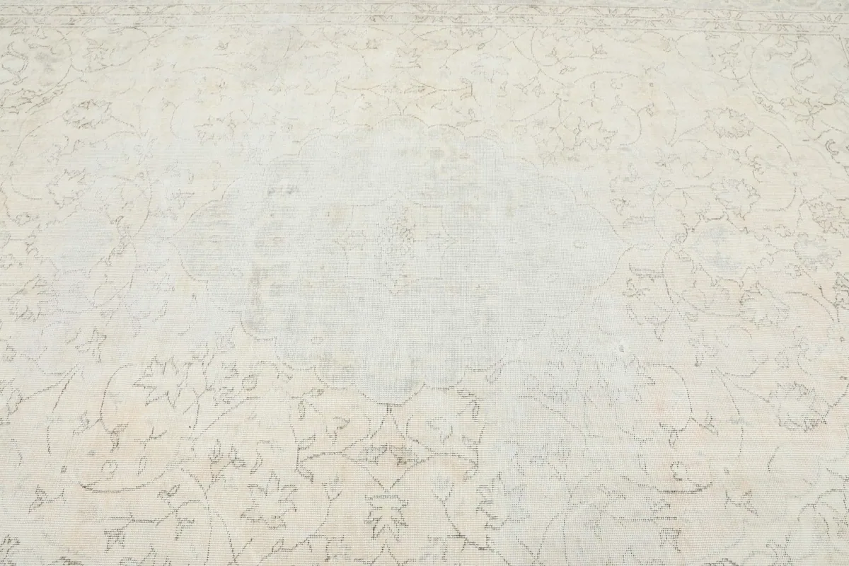 Overhead view focusing on the central field and faded motifs of the ivory and gray area rug