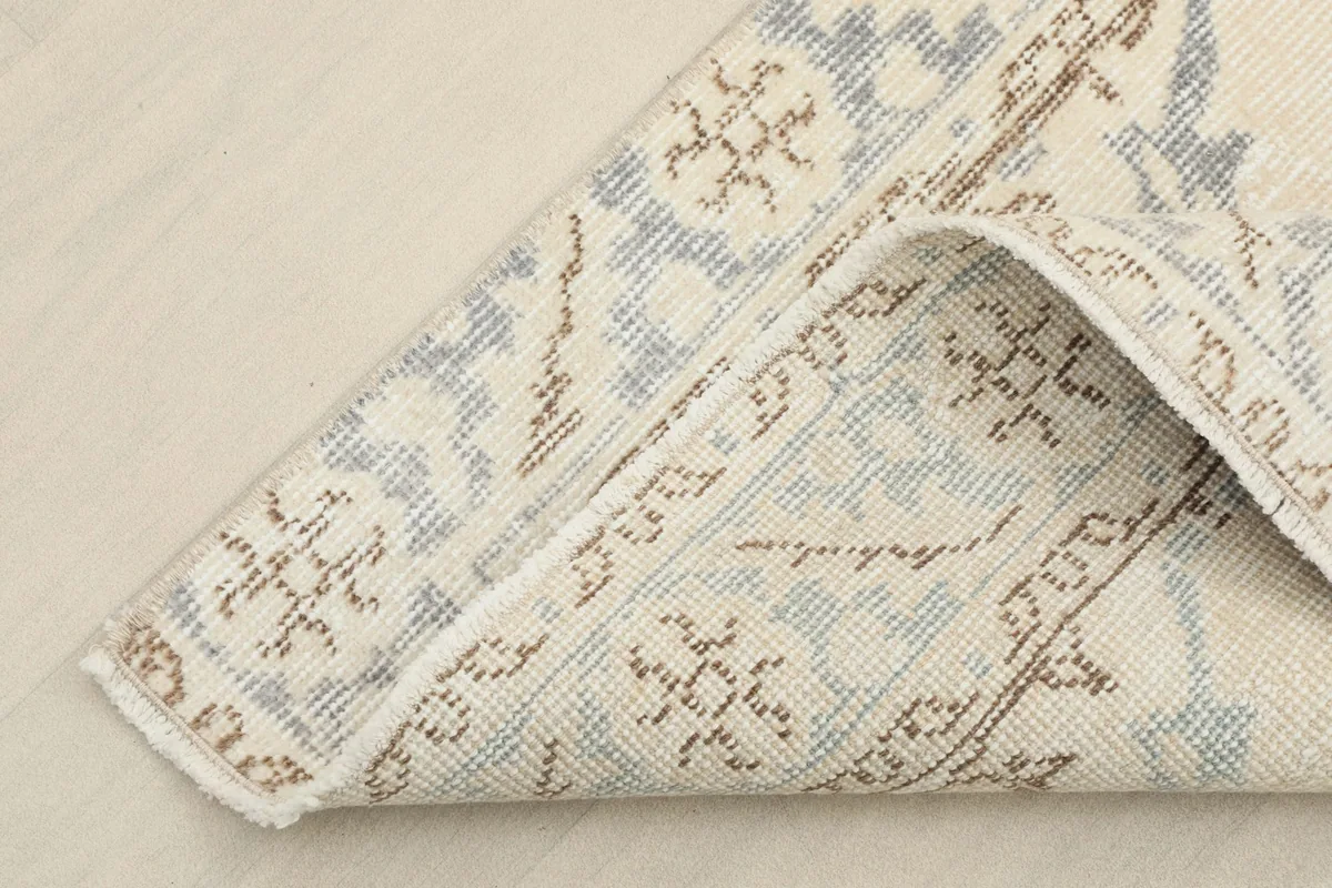Corner of the rug folded back, revealing the wool pile and cotton foundation construction.