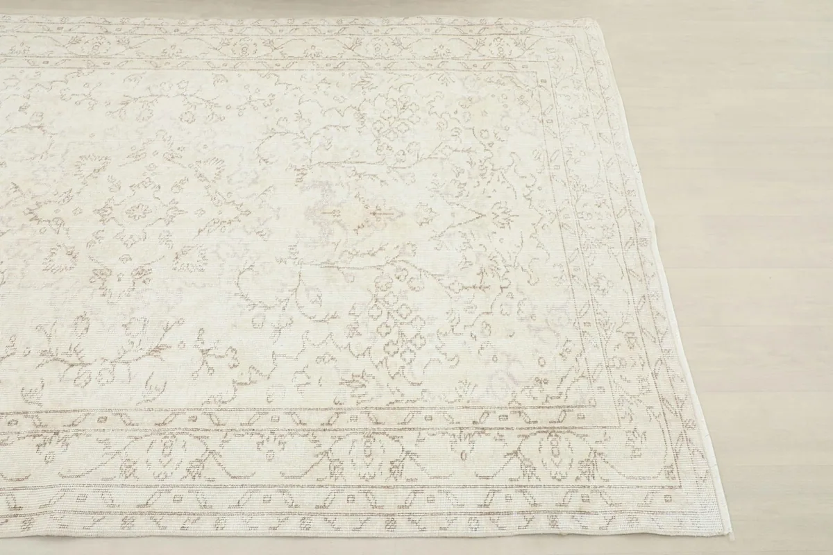 Close-up angled view of a corner of the ivory Anatolian rug, showing the faded design and border.