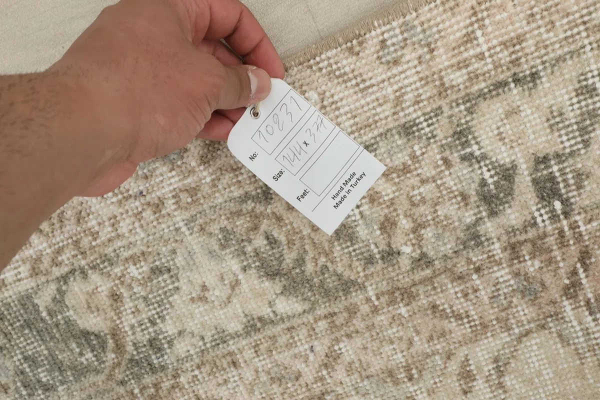 Hand holding a tag showing details of the vintage hand-knotted wool rug