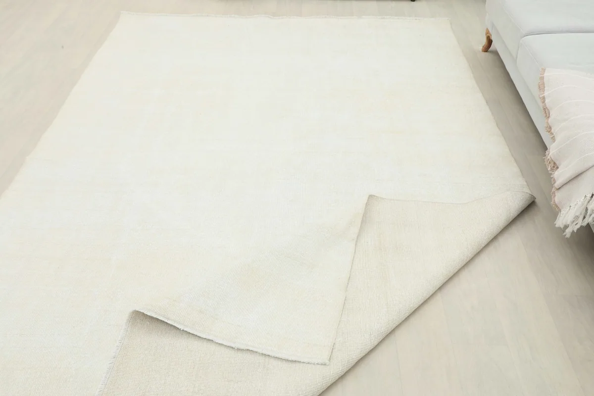 The cream rug partially folded back, revealing the neatly woven cotton foundation underneath.