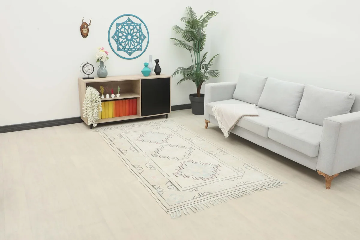The ivory and beige geometric rug placed in a living room setting with a light gray sofa and wooden cabinet.