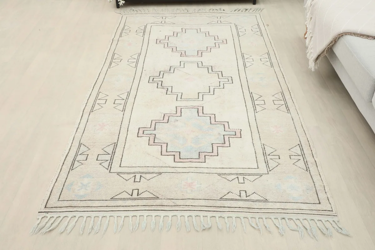 Full view of the ivory and beige geometric Anatolian rug laid out in a room, next to a sofa.
