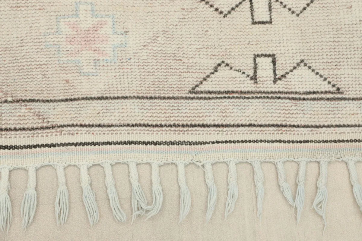 Close-up of the hand-knotted fringe and the edge of the ivory wool pile rug.
