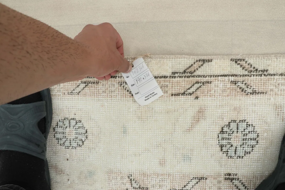 Hand holding a tag near the edge of the rug, showing the back of the hand-knotted weave.