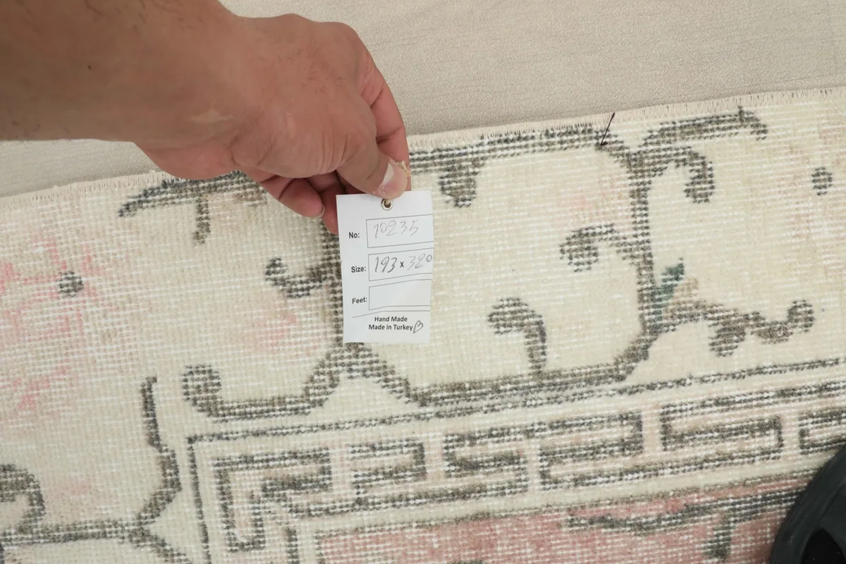 Hand holding a tag with size information (193 x 321 cm) near the rug's border.