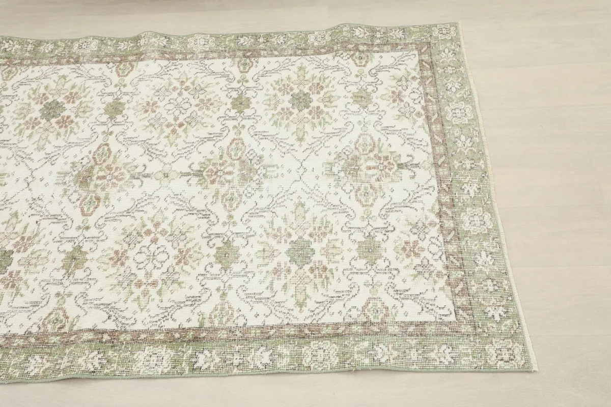 Close-up detail of the cream field and green border of the hand-knotted rug from an overhead angle