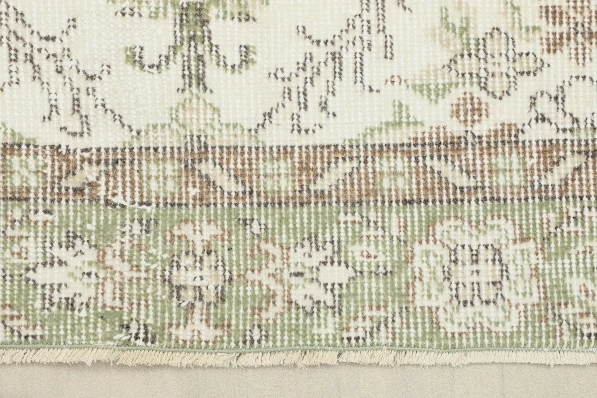 Close-up of the rug's green and tan border design, showing the distinct patterns and natural fringe