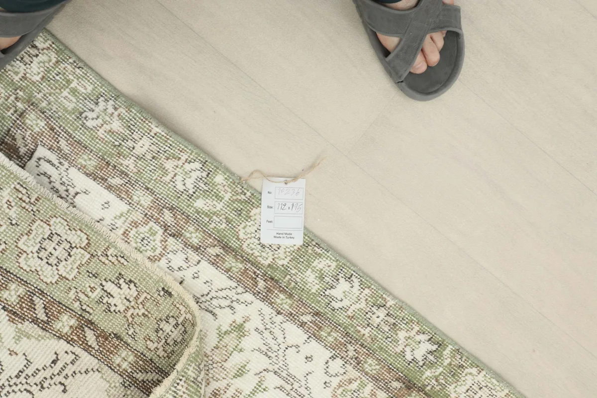 Overhead view of the rug with a size tag visible, next to a person's feet for scale