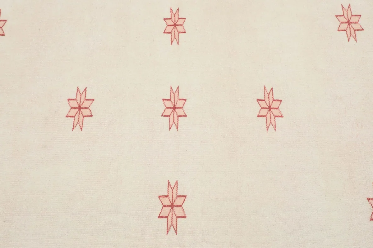 Close-up detail of the repeated red geometric star motifs on the ivory field.