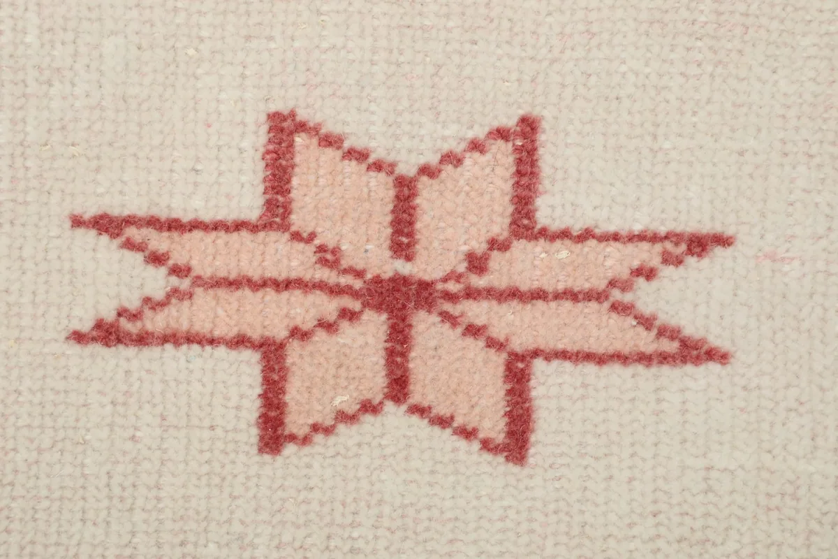 Macro detail of a single red geometric star motif, showing the hand-knotted wool pile.