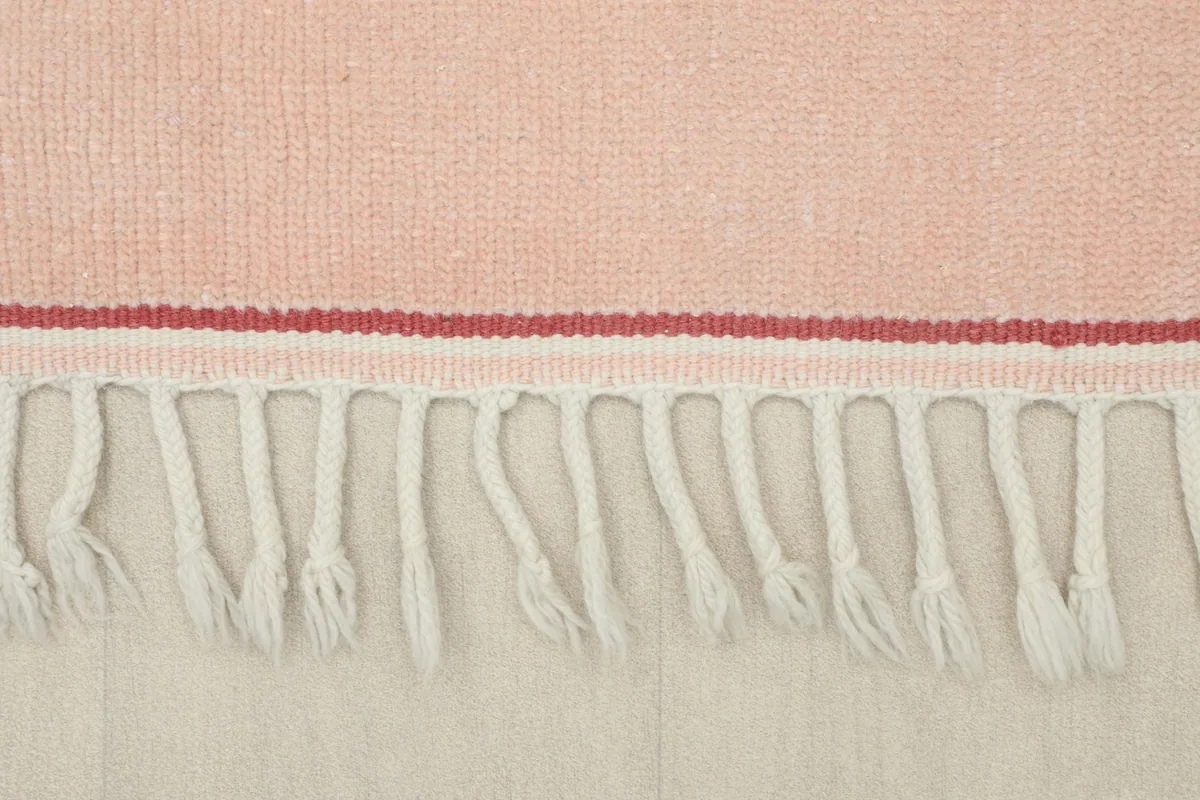Detail of the rug's short, natural fringe and the finished edge of the pink border.