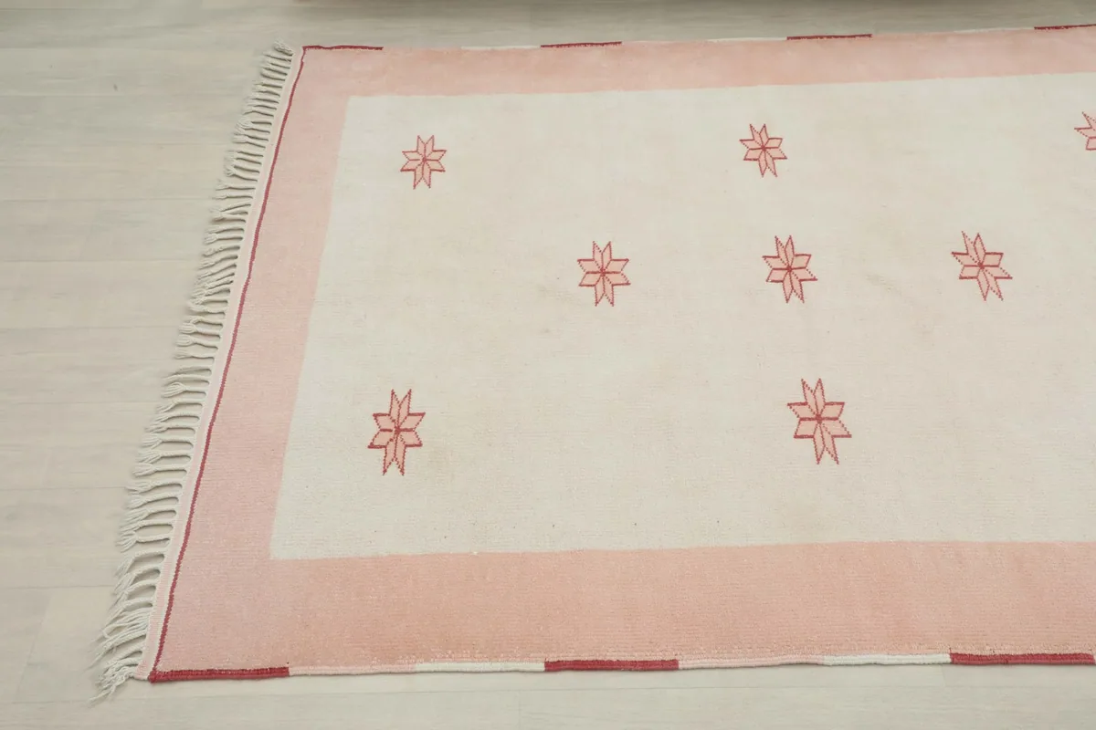 Overhead view focusing on one end of the rug, showing the pink border and ivory field with motifs.