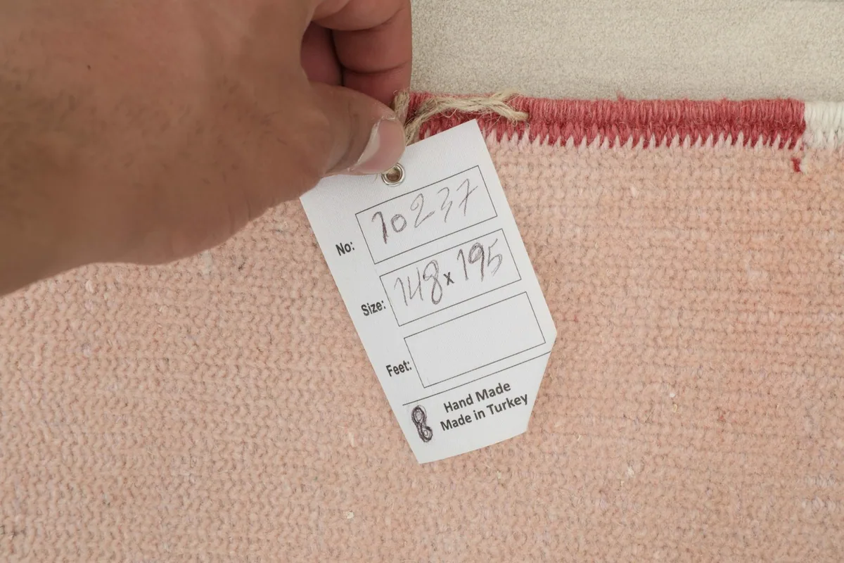 Hand holding a tag indicating the rug's number and size in centimeters, 148 x 195 cm.