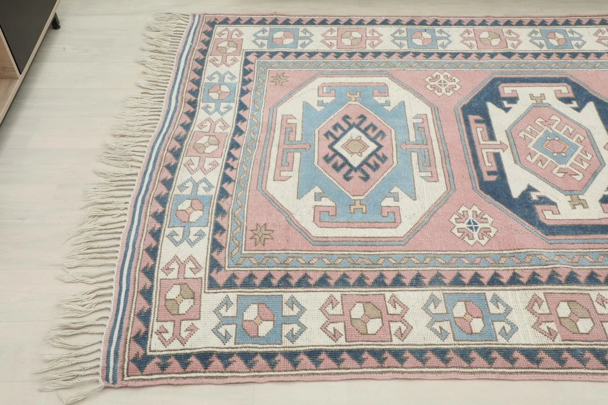 Close-up angled view of the top left corner of the pink and blue Anatolian rug, showing fringe
