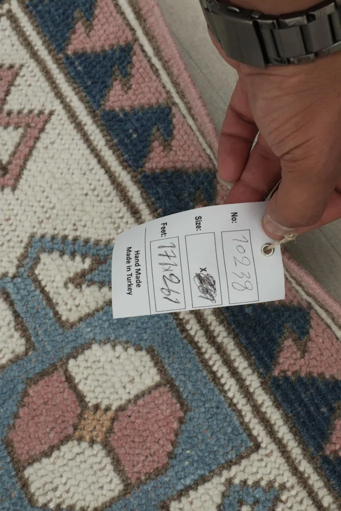 Hand holding a tag showing the rug's dimensions in centimeters and 'Hand Made in Turkey'