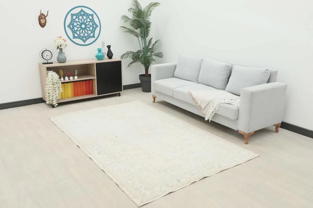 Cream vintage area rug displayed in a living room setting next to a gray sofa and console table.