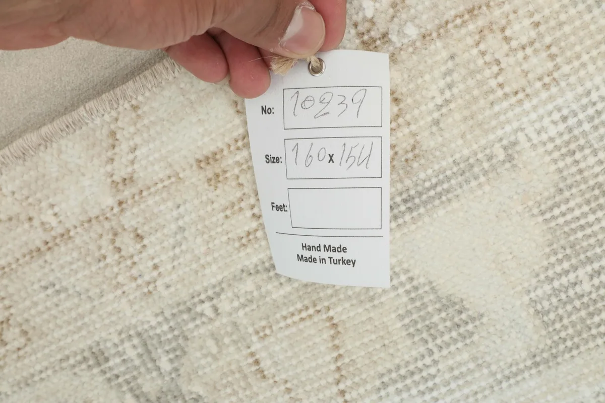 Hand holding a tag showing rug details and 'Hand Made in Turkey' on the reverse side of the rug.