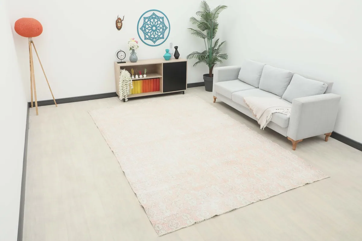 Large rose and beige floral vintage rug placed in a living room setting with a light gray couch.