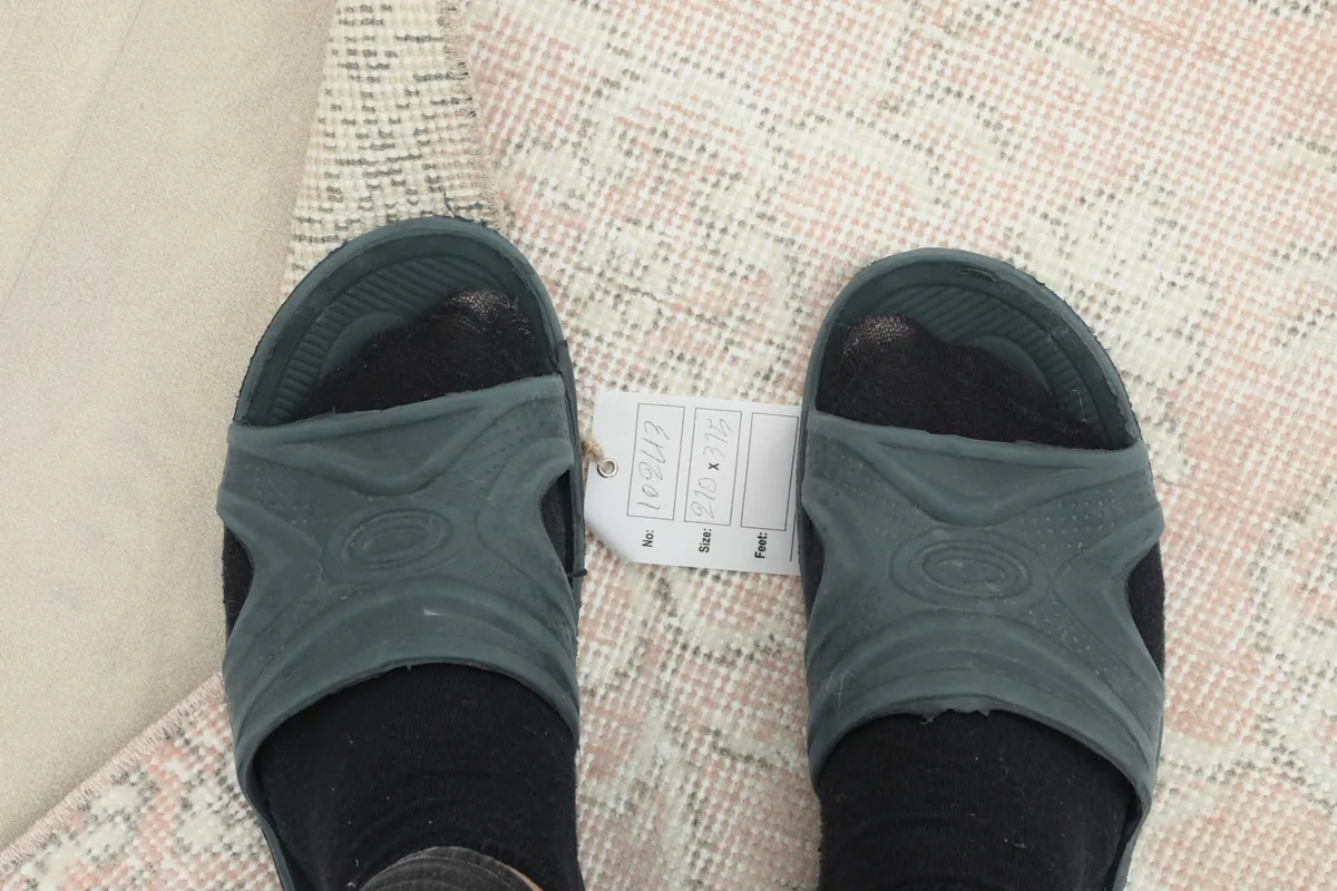 Feet in sandals next to a size tag, providing a sense of scale for the rug's pattern and pile.