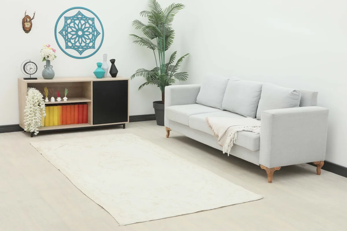 Vintage ivory and tan area rug placed in a living room setting with a light gray sofa and wooden cabinet.