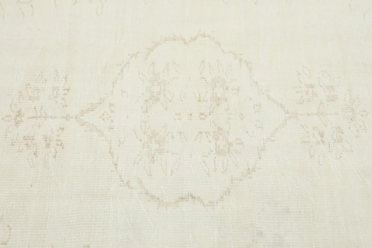 Detailed shot of the central medallion design, showcasing the delicate, worn tan motifs against the ivory.