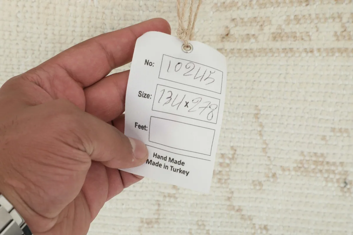 A hand holding a tag showing the rug's number and size in centimeters, confirming its origin from Turkey.