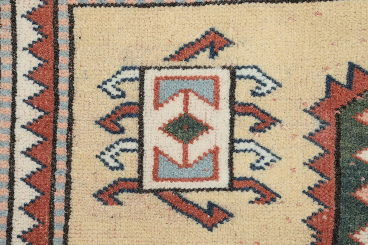 Detailed close-up of a tribal geometric motif within the rug's beige field, showing individual knots.